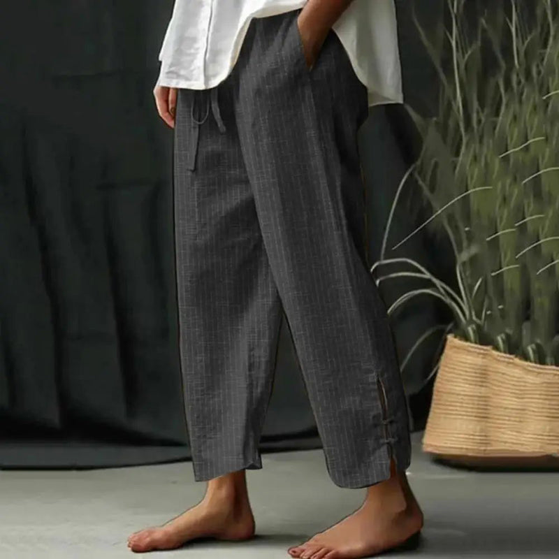 Woman wearing tapered drawcord-waist pants with sandals, standing in a sunlit garden.