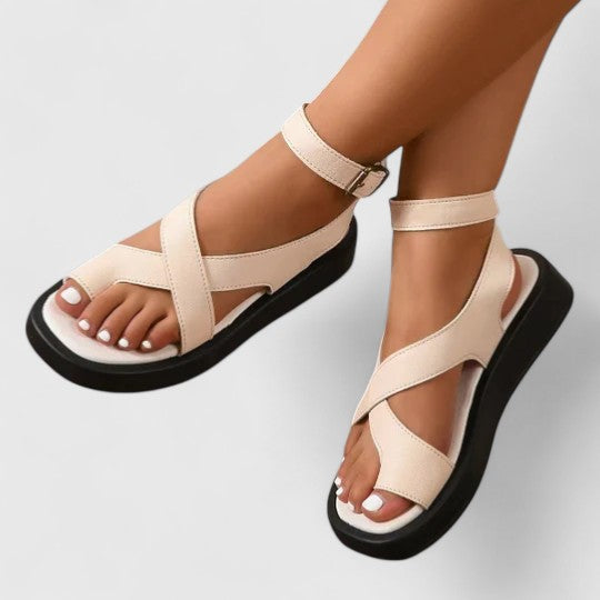 A woman walking comfortably in beige cushioned cross-strap sandals with an adjustable ankle buckle.