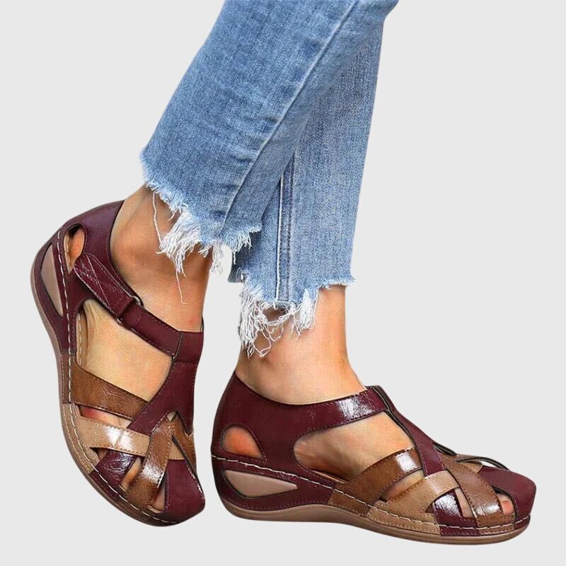 A woman wearing burgundy and brown woven closed-toe wedge sandals with side cutouts, walking with ease