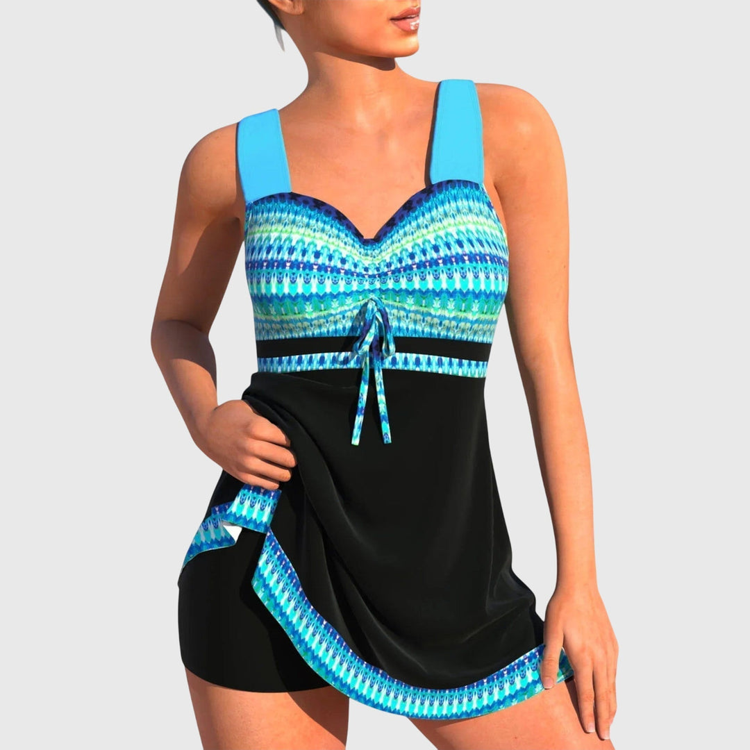 A woman on the beach in a colourful skirted swimsuit with a printed bodice and soft swim skirt, smiling in the sun.