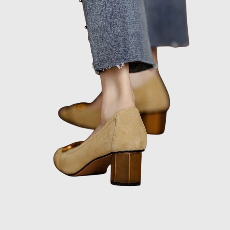 A woman wearing khaki block-heel court shoes with a gold buckle detail, standing with ease and confidence.
