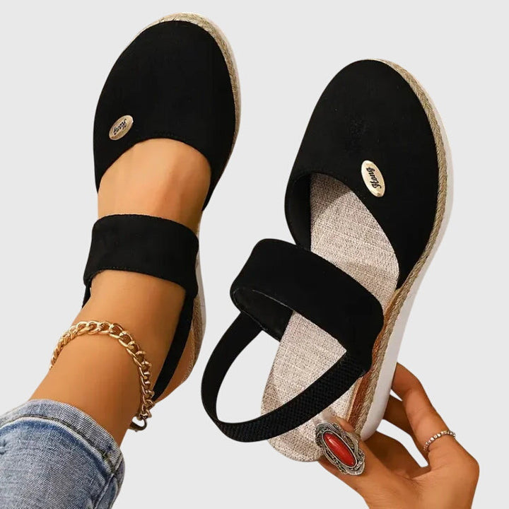 Black closed-toe wedge espadrilles with a wide stretch strap and a braided-trim platform wedge.