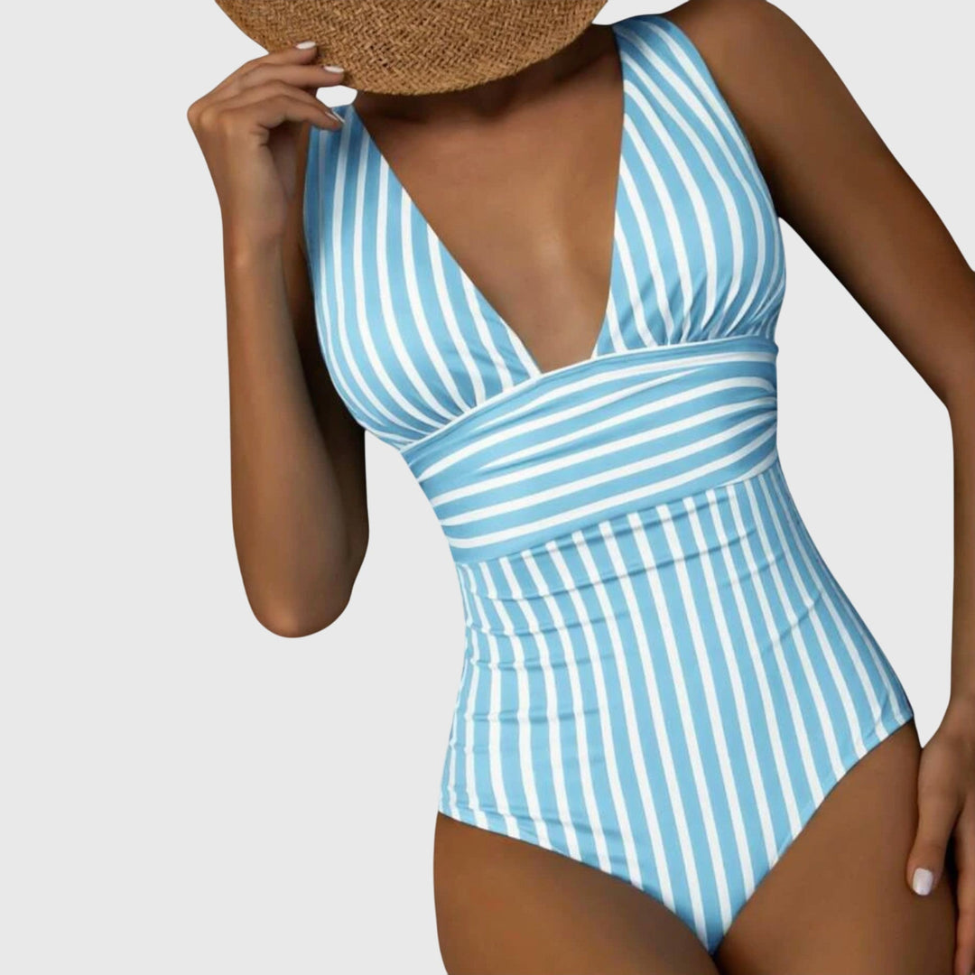 A woman by the sea in a beige and white striped V-neck swimsuit, relaxed and glowing in the sun.