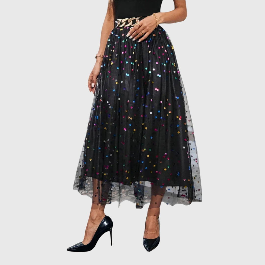A woman in a black pleated skirt covered in multicoloured sparkling confetti dots, styled for an evening out.
