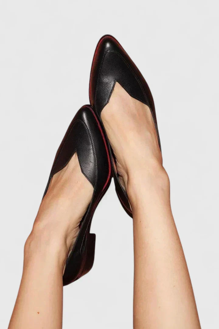 A pair of sleek black pointed-toe d'Orsay flats with curved side cutouts, worn without socks.