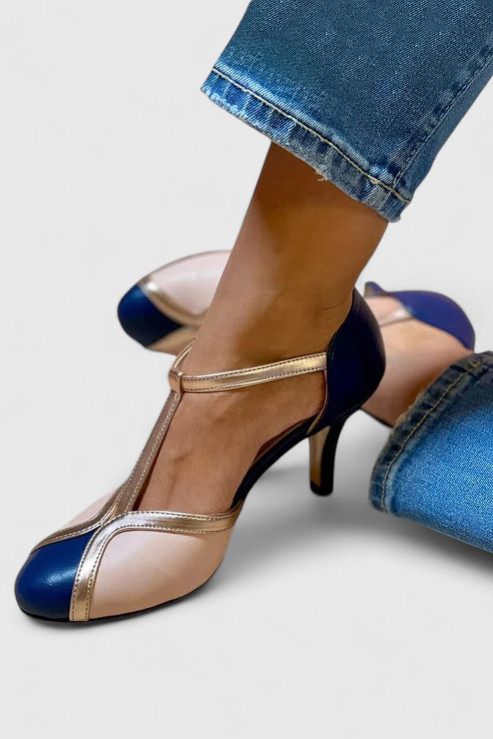 A woman wearing navy, blush and gold T-strap heels with a rounded toe, paired with jeans.