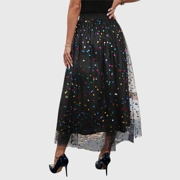 A woman in a black pleated skirt covered in multicoloured sparkling confetti dots, styled for an evening out.