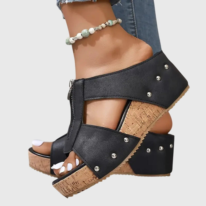 A woman wearing black zip-front wedge mules with a cushioned footbed and a broad platform sole.