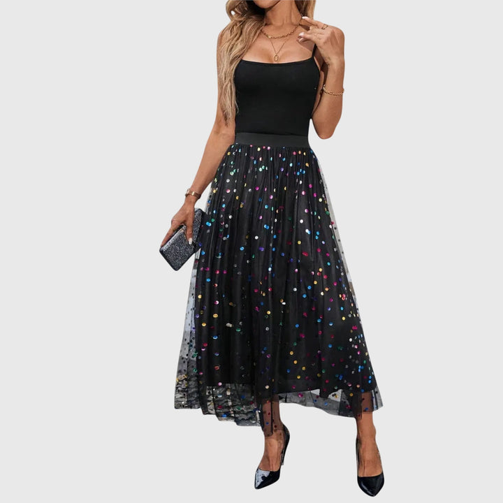 A woman in a black pleated skirt covered in multicoloured sparkling confetti dots, styled for an evening out.