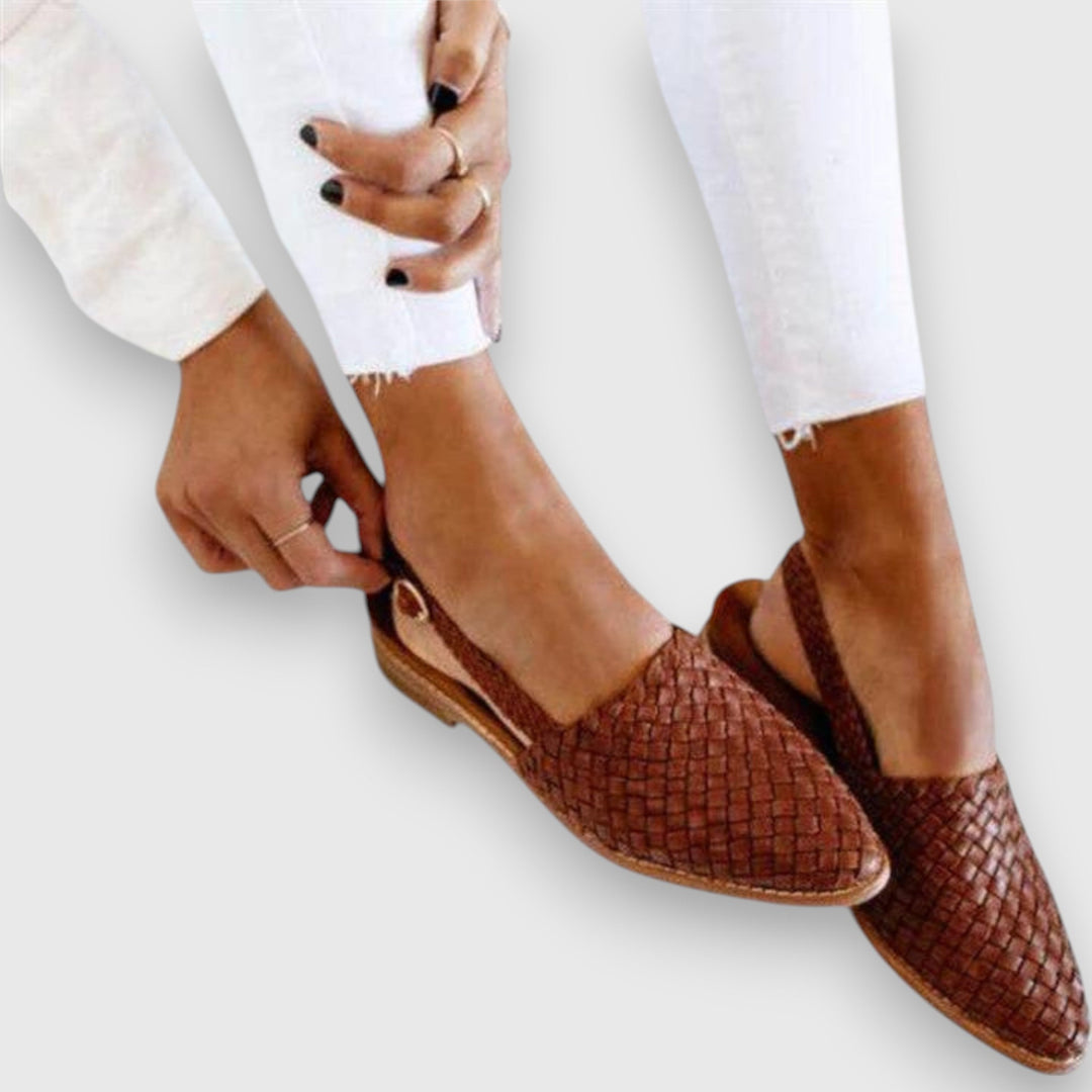 A woman wearing warm brown woven pointed-toe slingback flats with white cropped pants.