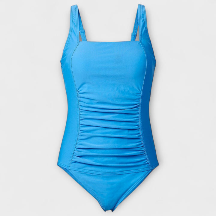A woman on the sand in a retro-style padded swimsuit, poised and confident in the sunshine.