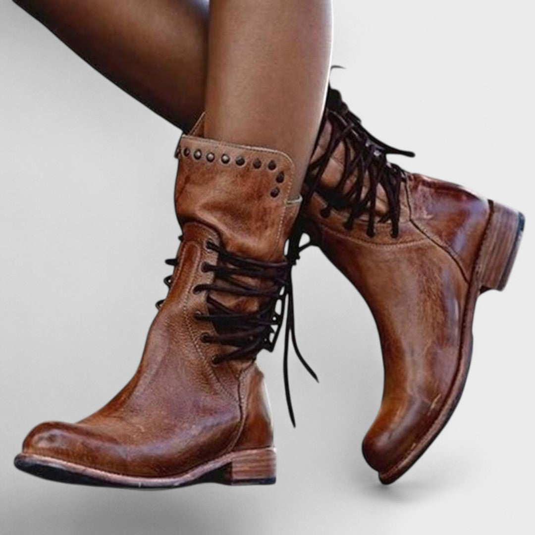 A woman in brown lace-up mid-calf boots walking steadily through town on a wet day.