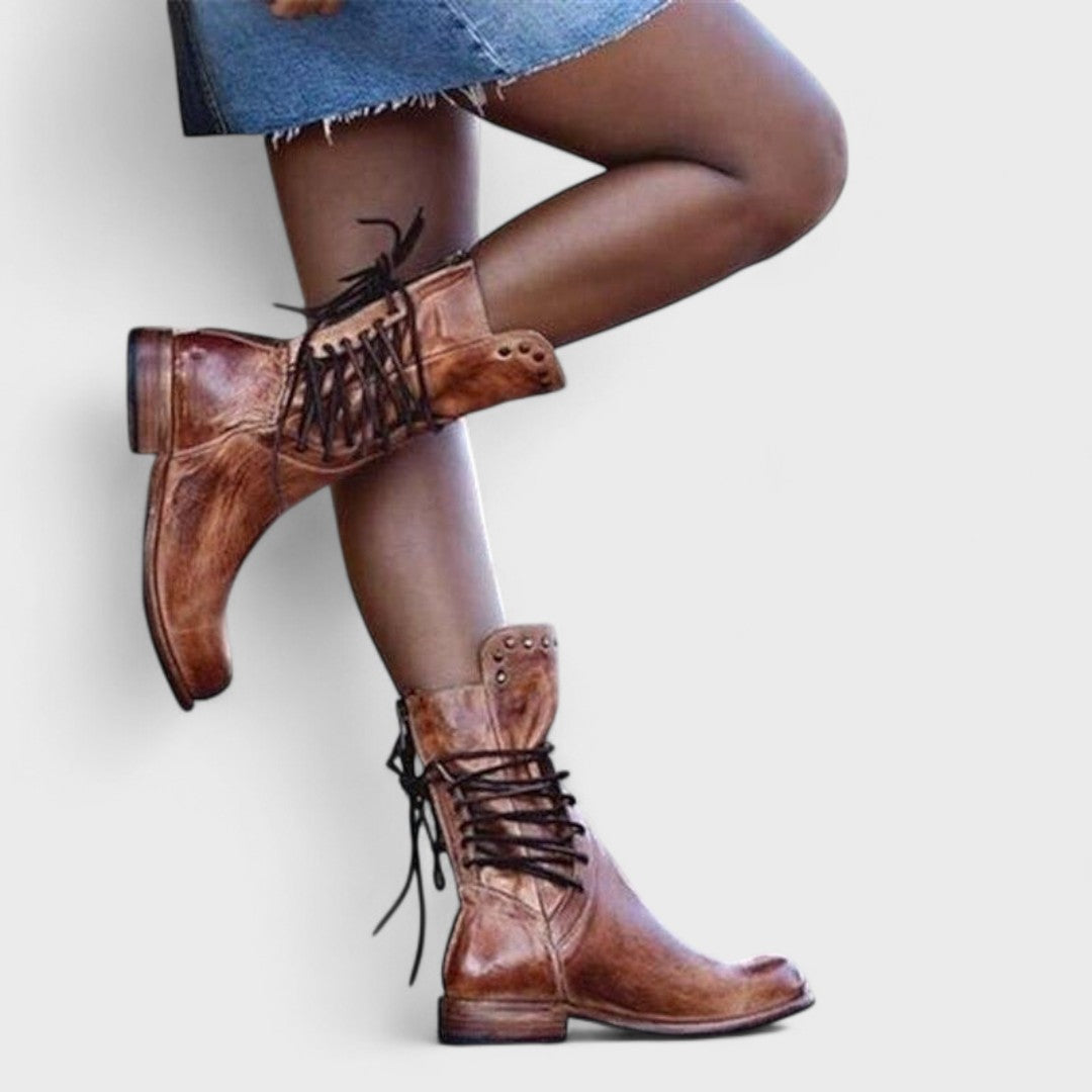 A woman in brown lace-up mid-calf boots walking steadily through town on a wet day.