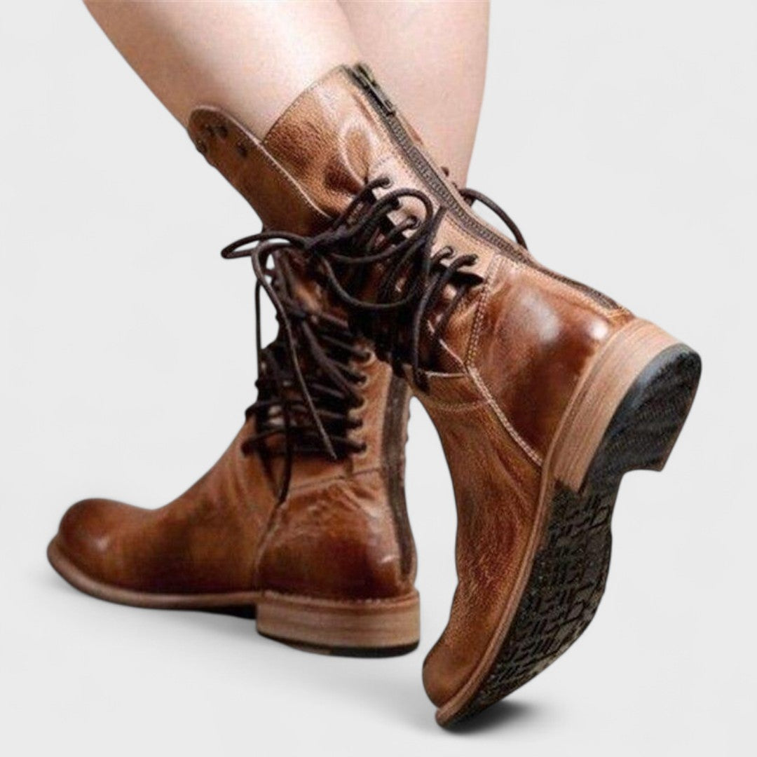 A woman in brown lace-up mid-calf boots walking steadily through town on a wet day.