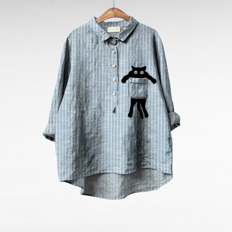 Woman wearing a grey striped summer blouse with a playful black cat motif on the pocket.