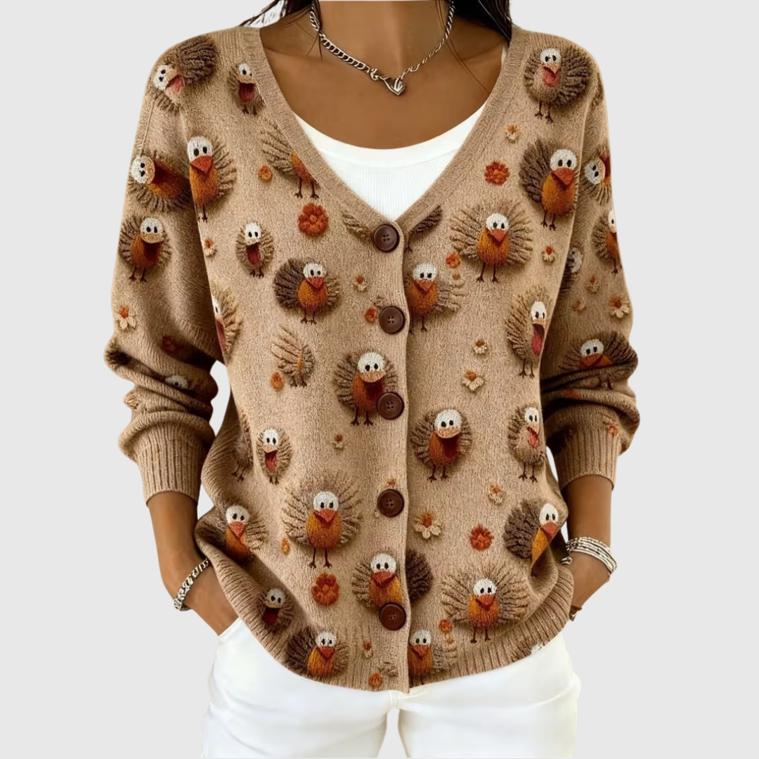 A woman wearing a camel buttoned cardigan covered in raised bird motifs, worn open over a white top.