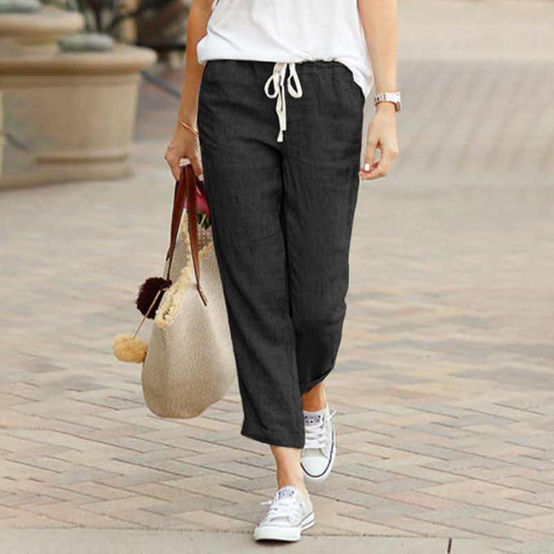 Woman wearing flared drawcord-waist pants with sneakers, walking through town.