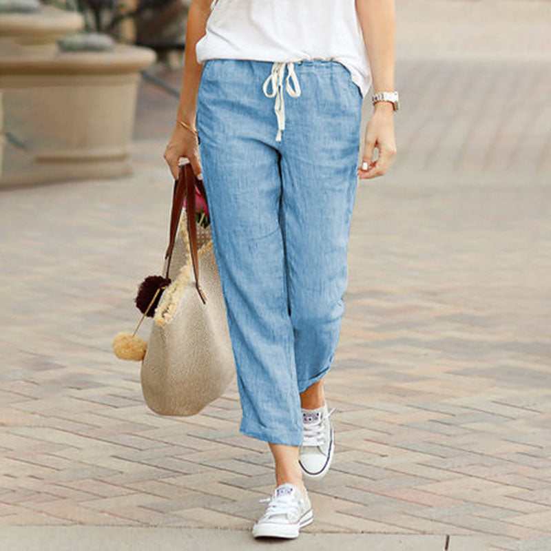 Woman wearing flared drawcord-waist pants with sneakers, walking through town.