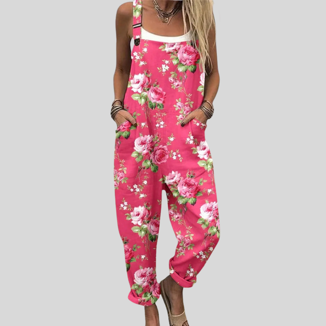 Woman wearing bold pink overalls printed with white and pink roses and green leaves, standing and smiling.