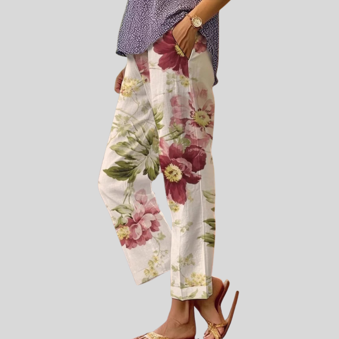 Woman wearing cream pants with a large red and pink floral print, with sandals.