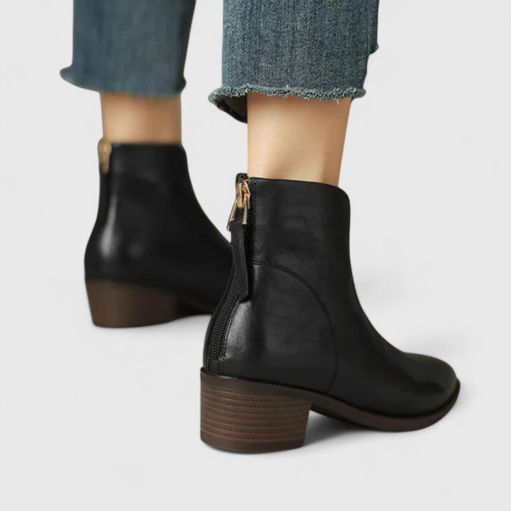 Woman wearing black elegant boots with tailored pants on a city footpath.