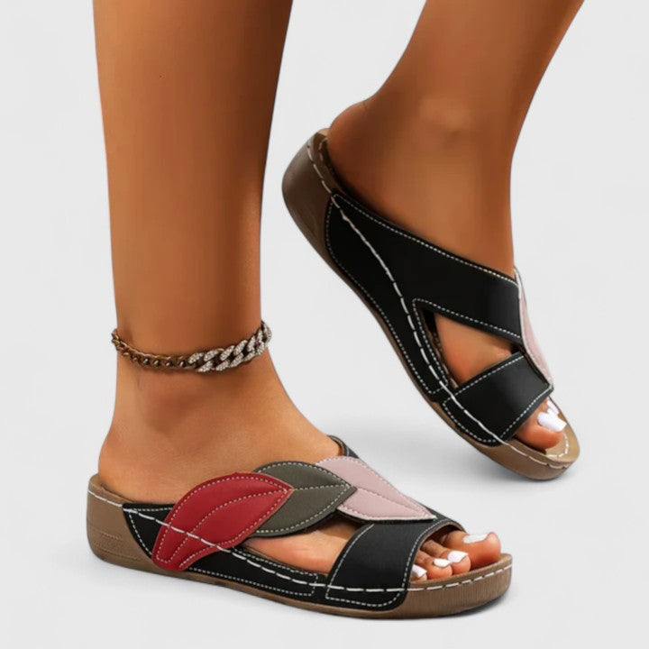 A woman wearing colourful leaf-print sandals with a cushioned insole and easy slip-on design.