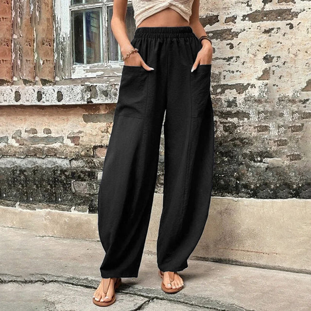 A woman walking in flowing wide-leg pants with big patch pockets and an elegant, draped silhouette.