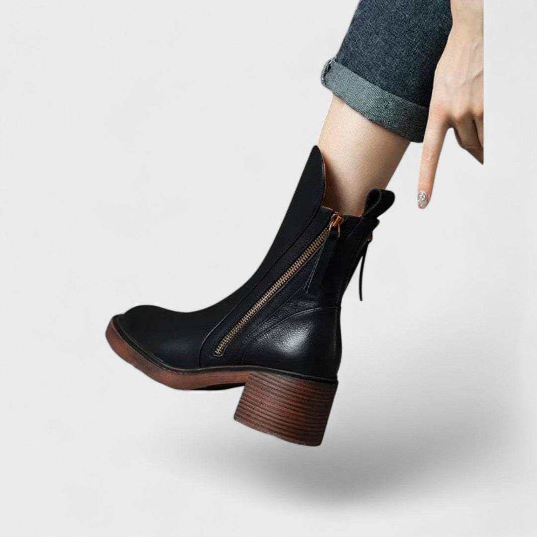 Woman wearing black refined ankle boots with tailored pants in a city setting.