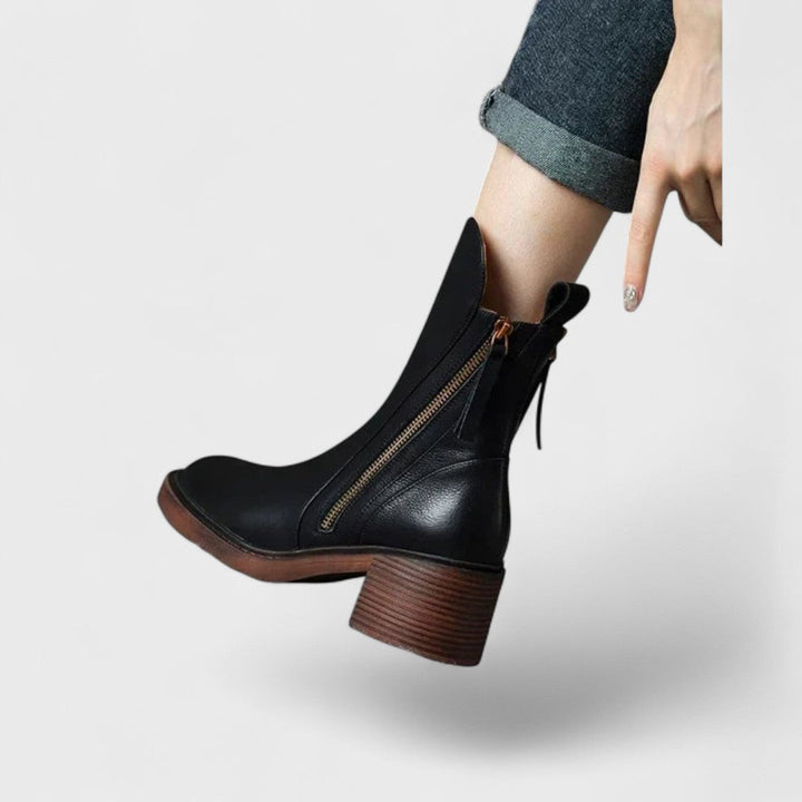 Woman wearing black refined ankle boots with tailored pants in a city setting.
