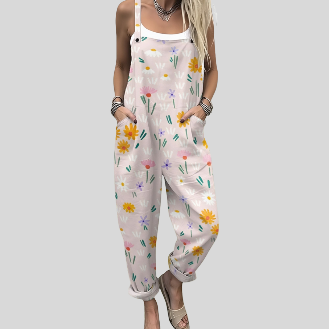 A woman wearing soft pink overalls printed with scattered daisies and wildflowers, smiling in a park.