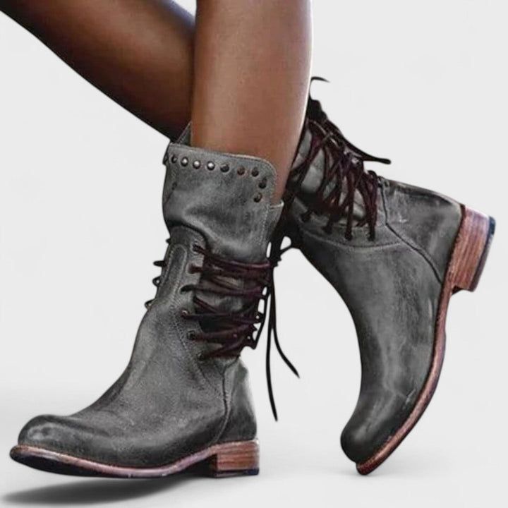 A woman in brown lace-up mid-calf boots walking steadily through town on a wet day.