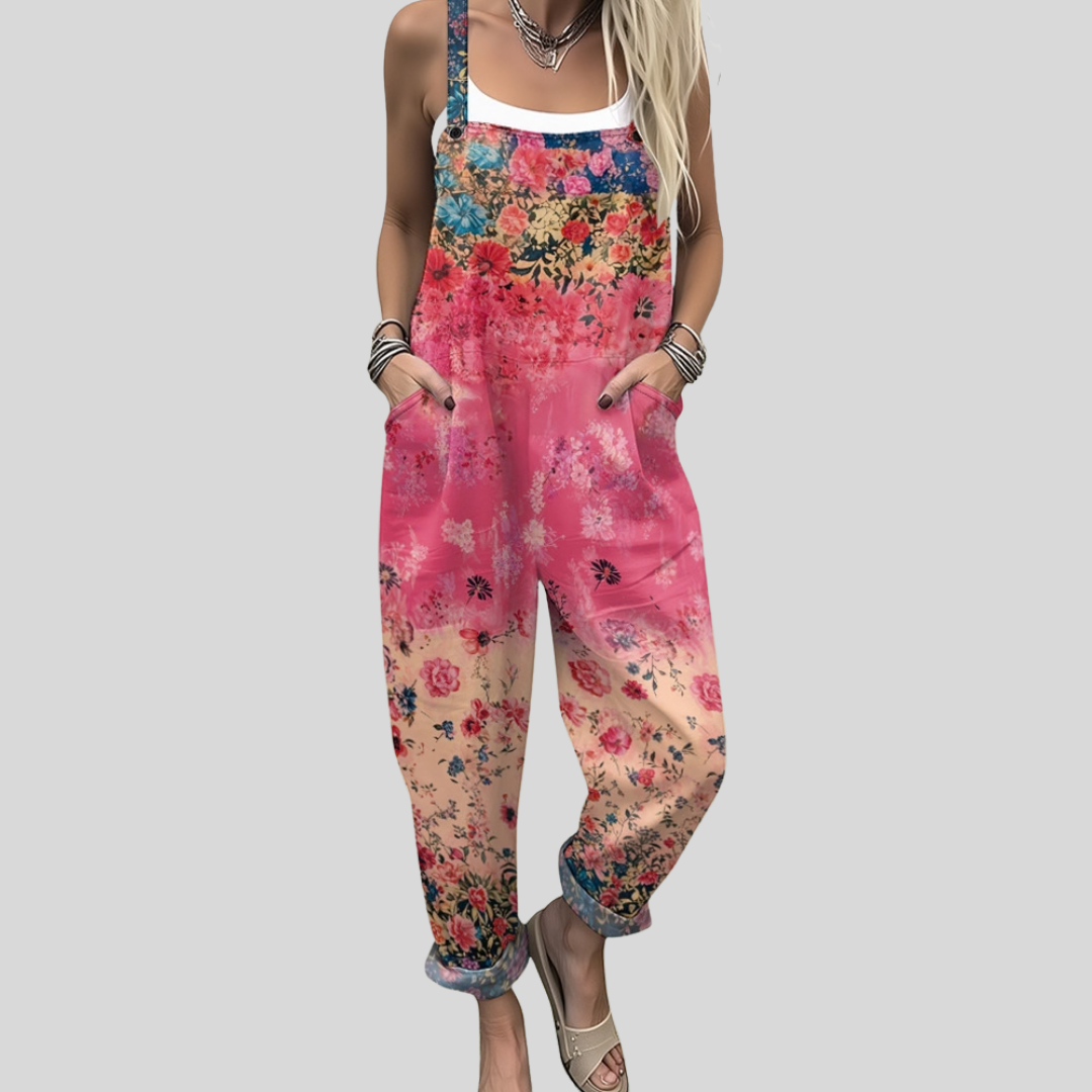 A woman wearing overalls with a warm coral and pink floral print, smiling in a summer garden.