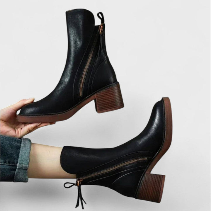 Woman wearing black refined ankle boots with tailored pants in a city setting.