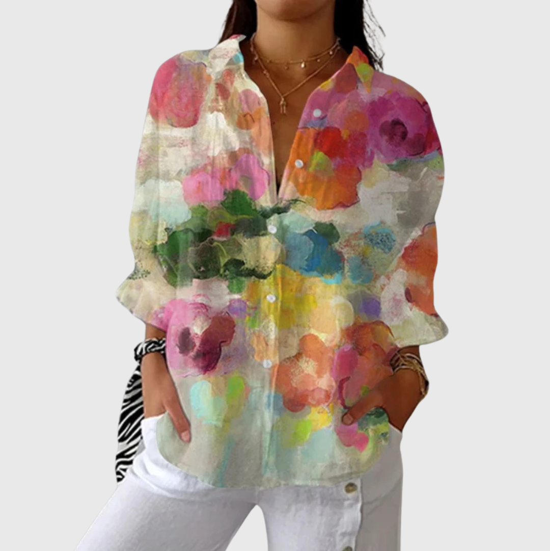 A woman wearing a colourful floral blouse worn loosely with jeans, smiling
