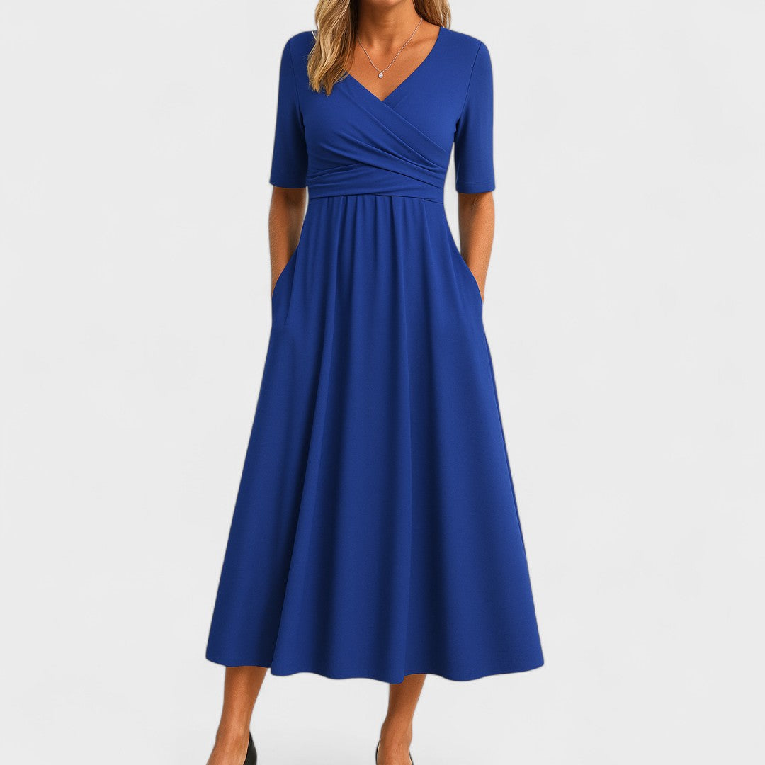 Woman wearing a royal blue mid-calf wrap dress with a crossover V-neckline, gathered waist, short sleeves and a gently flared skirt.