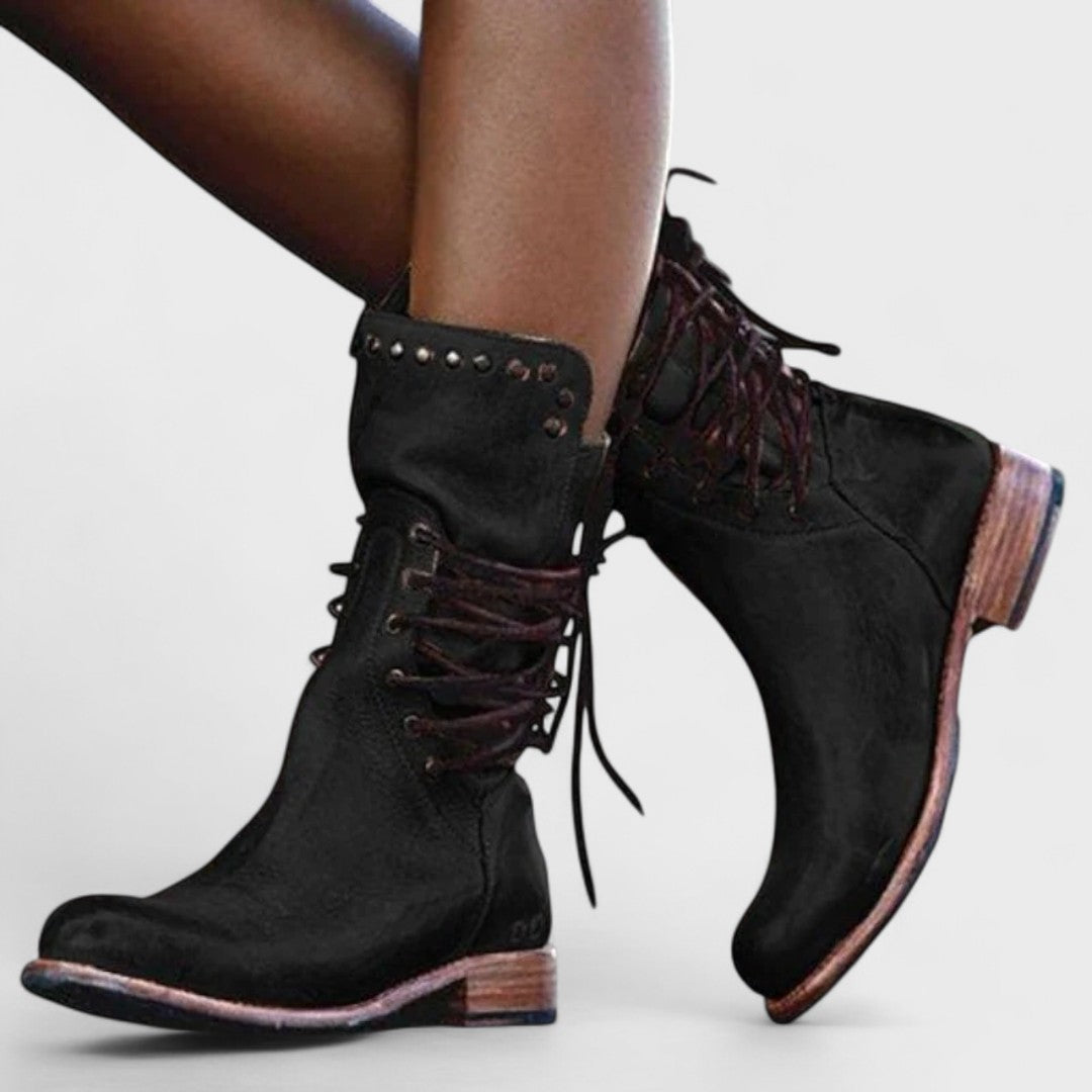 A woman in brown lace-up mid-calf boots walking steadily through town on a wet day.