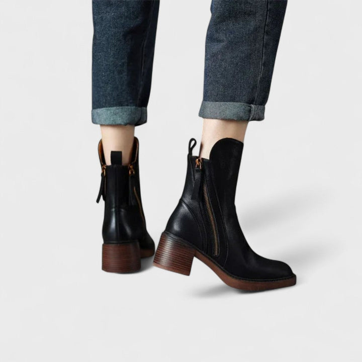 Woman wearing black refined ankle boots with tailored pants in a city setting.