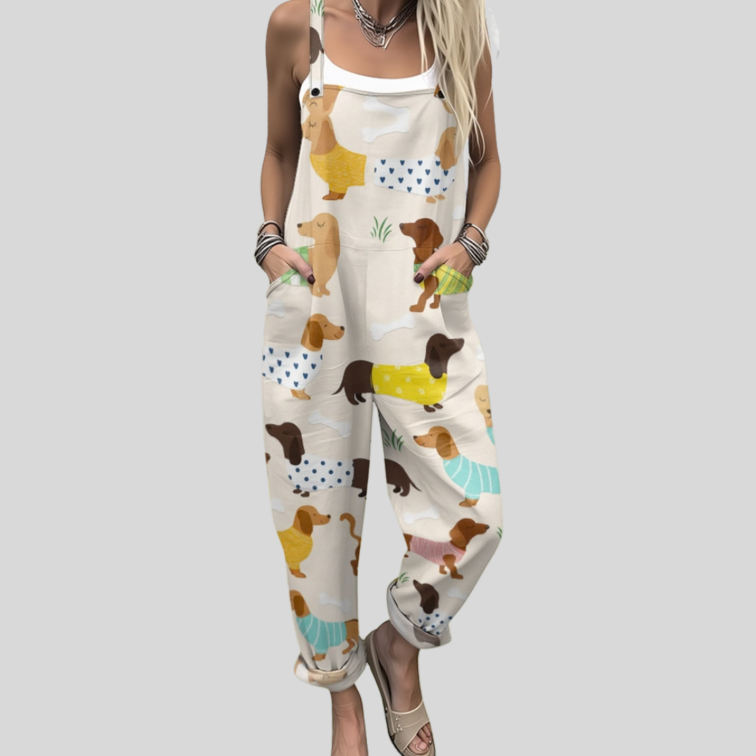 A woman wearing cream overalls printed with little dachshunds in colourful sweaters, smiling brightly.