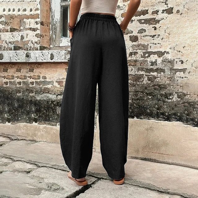 A woman walking in flowing wide-leg pants with big patch pockets and an elegant, draped silhouette.