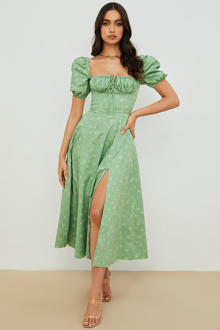 A woman wearing a floral midi dress with puff sleeves and a tie-front bodice, standing in the sunshine.