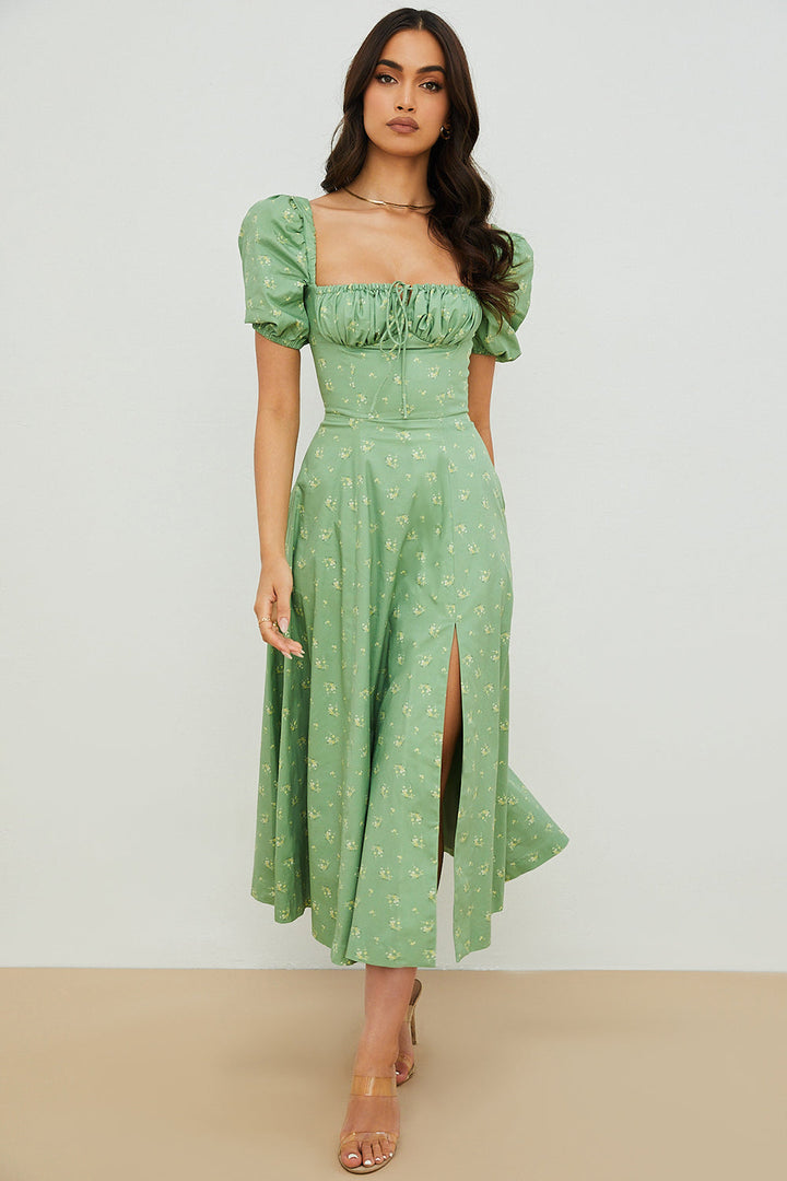A woman wearing a floral midi dress with puff sleeves and a tie-front bodice, standing in the sunshine.