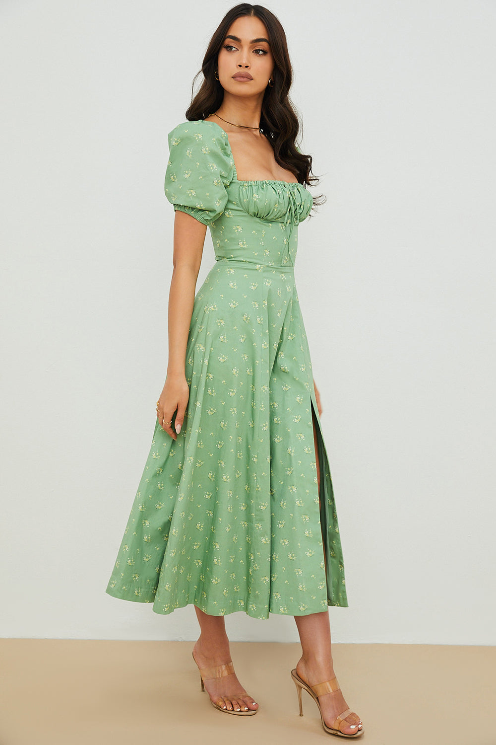 A woman wearing a floral midi dress with puff sleeves and a tie-front bodice, standing in the sunshine.