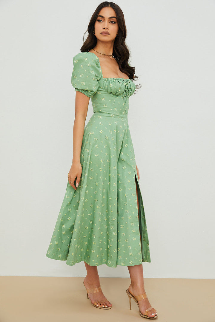 A woman wearing a floral midi dress with puff sleeves and a tie-front bodice, standing in the sunshine.