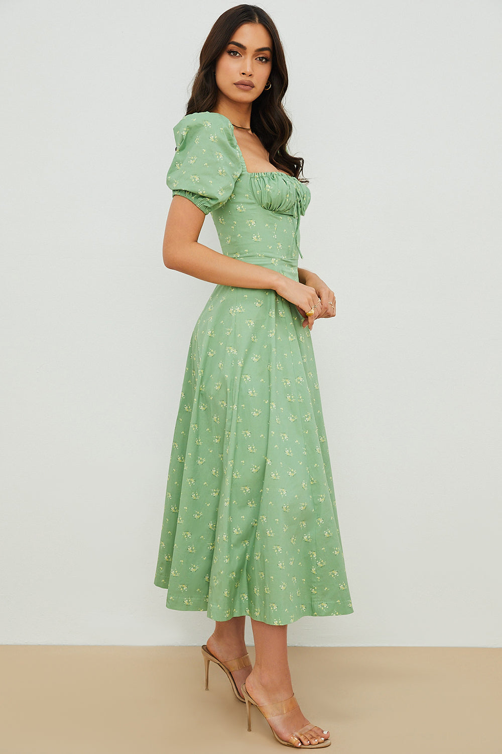 A woman wearing a floral midi dress with puff sleeves and a tie-front bodice, standing in the sunshine.