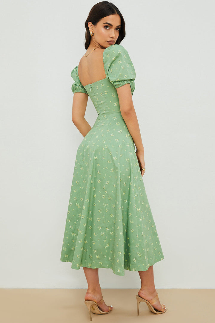 A woman wearing a floral midi dress with puff sleeves and a tie-front bodice, standing in the sunshine.