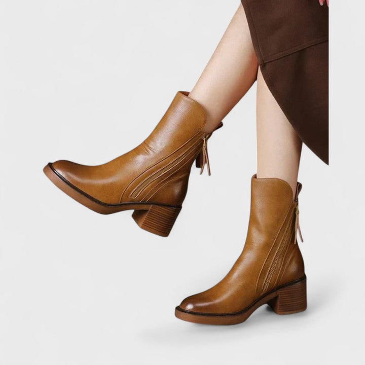 Woman wearing black refined ankle boots with tailored pants in a city setting.