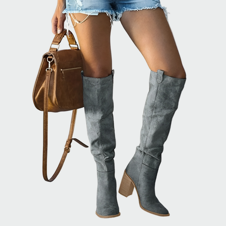 A woman in a dress wearing warm brown knee-high Western-style boots with a sturdy block heel.