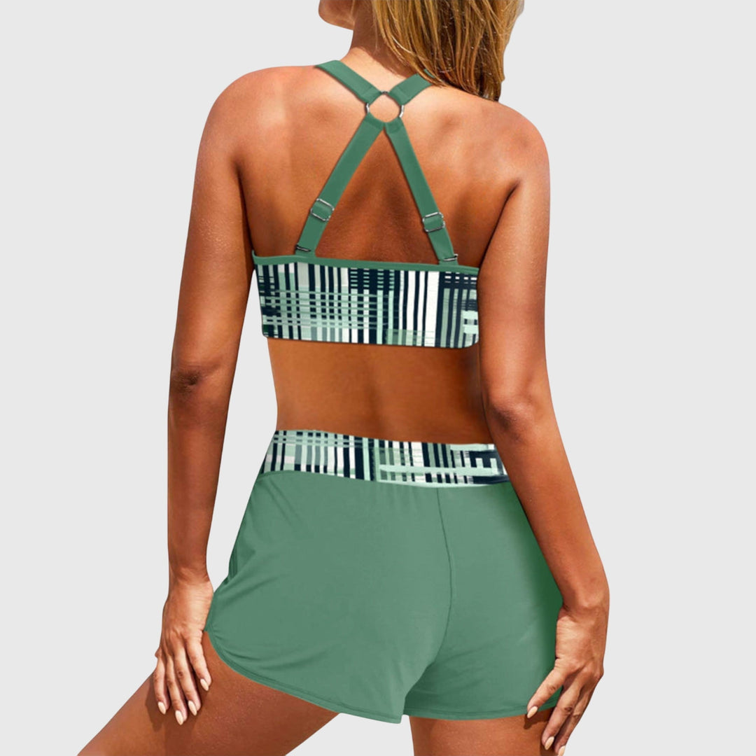A woman at the beach in a striped bikini top with matching swim shorts, confident and relaxed in the sun.