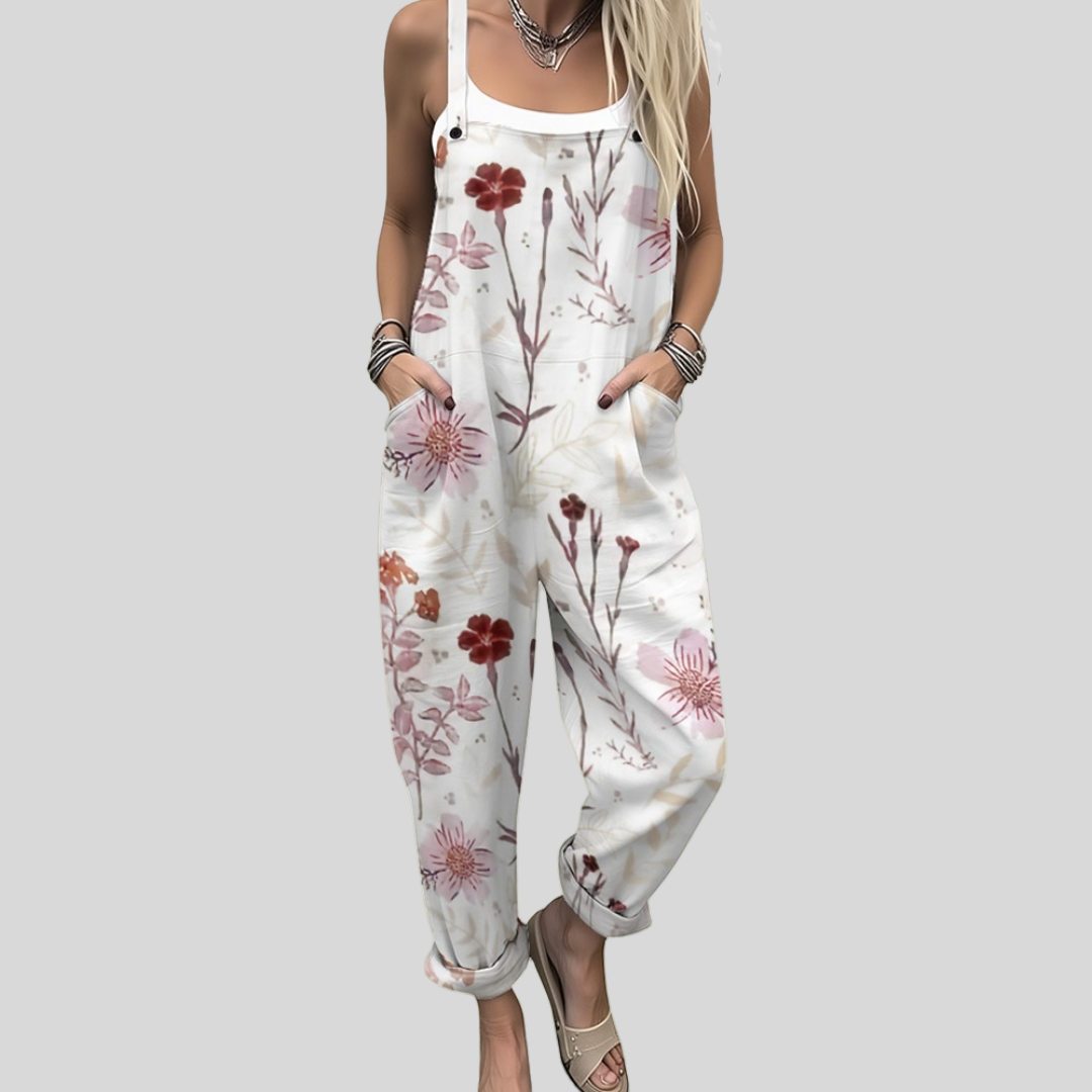 Woman wearing white overalls printed with fine branches and red and burgundy blossoms, standing elegantly.