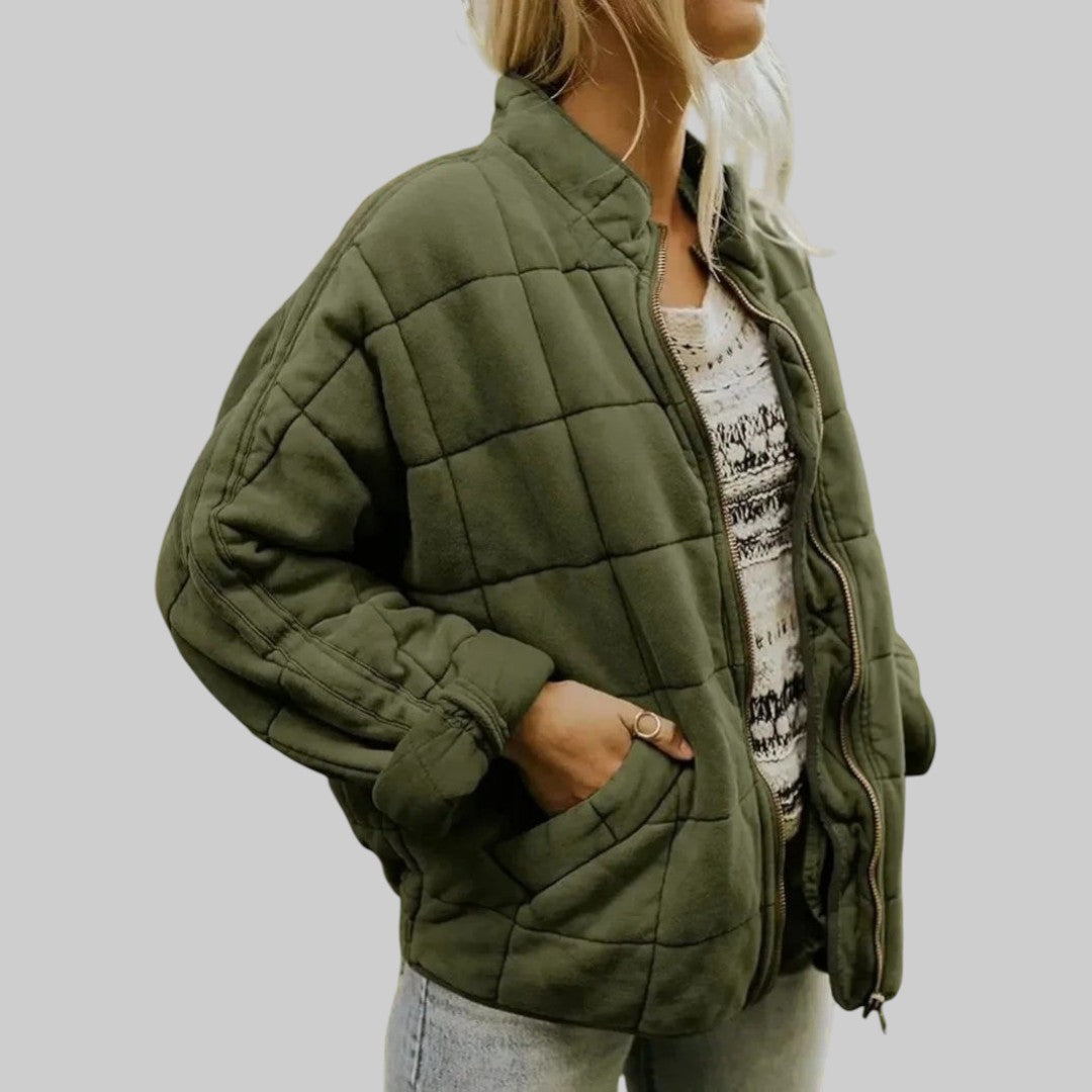 A woman wearing an oversized blush pink quilted jacket with a stand collar and zip front, hand in the pocket.